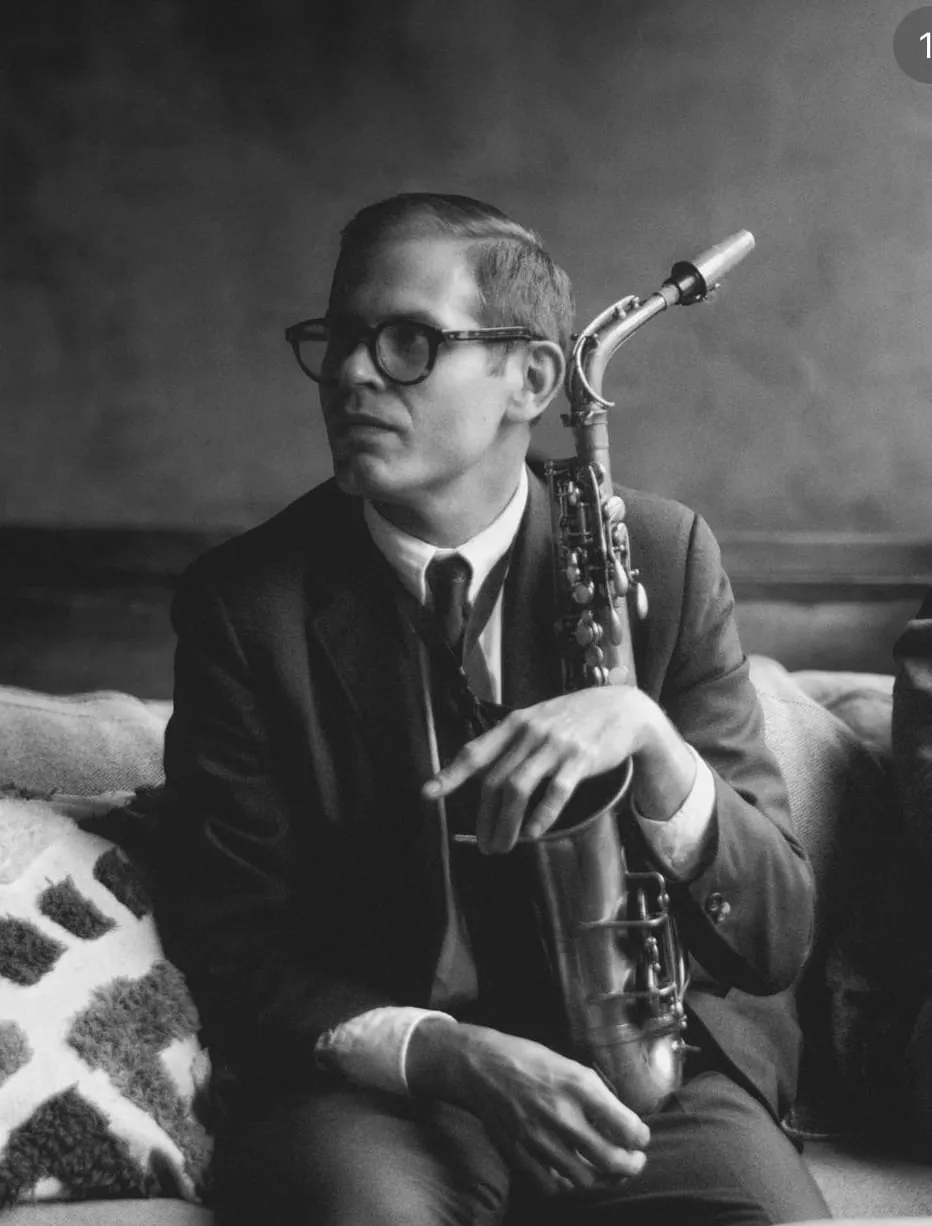 Black and white photograph of Aaron Johnson seated in a club with an alto saxophone across his lap.