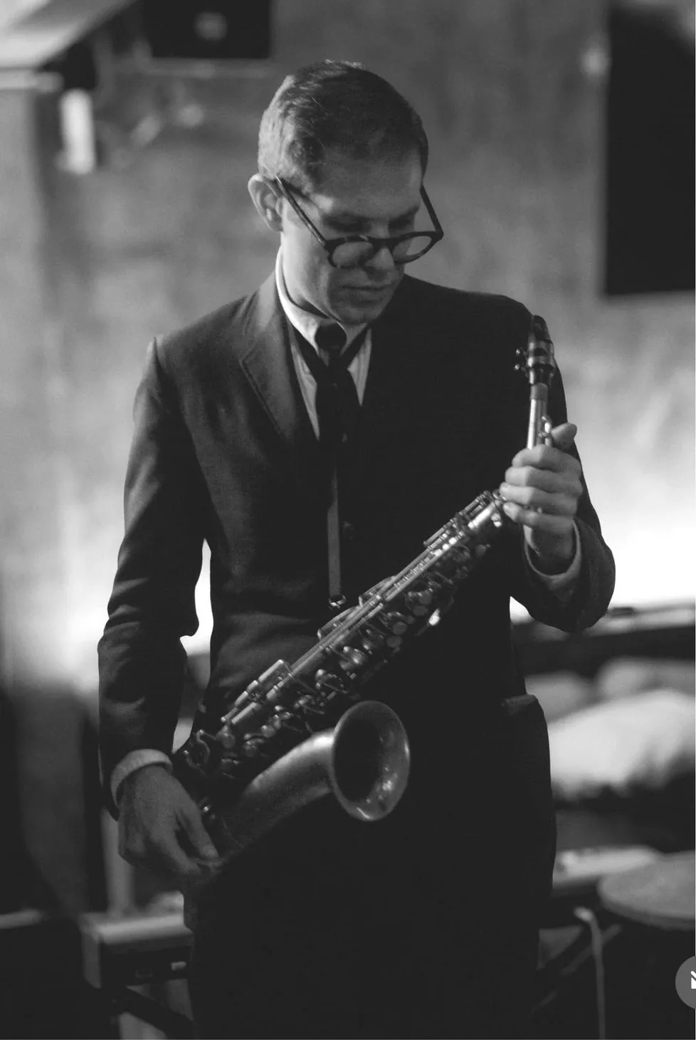 Aaron Johnson standing and playing alto saxophone in a dark club, in black and white.