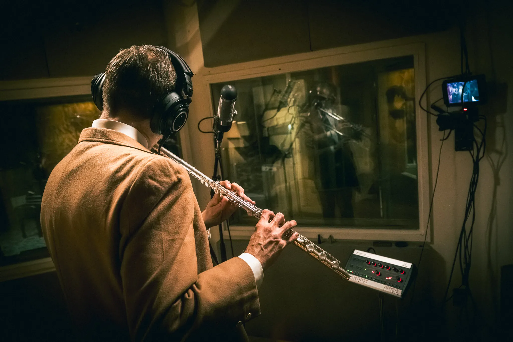 Aaron Johnson photographed from behind playing flute, facing the control room window.