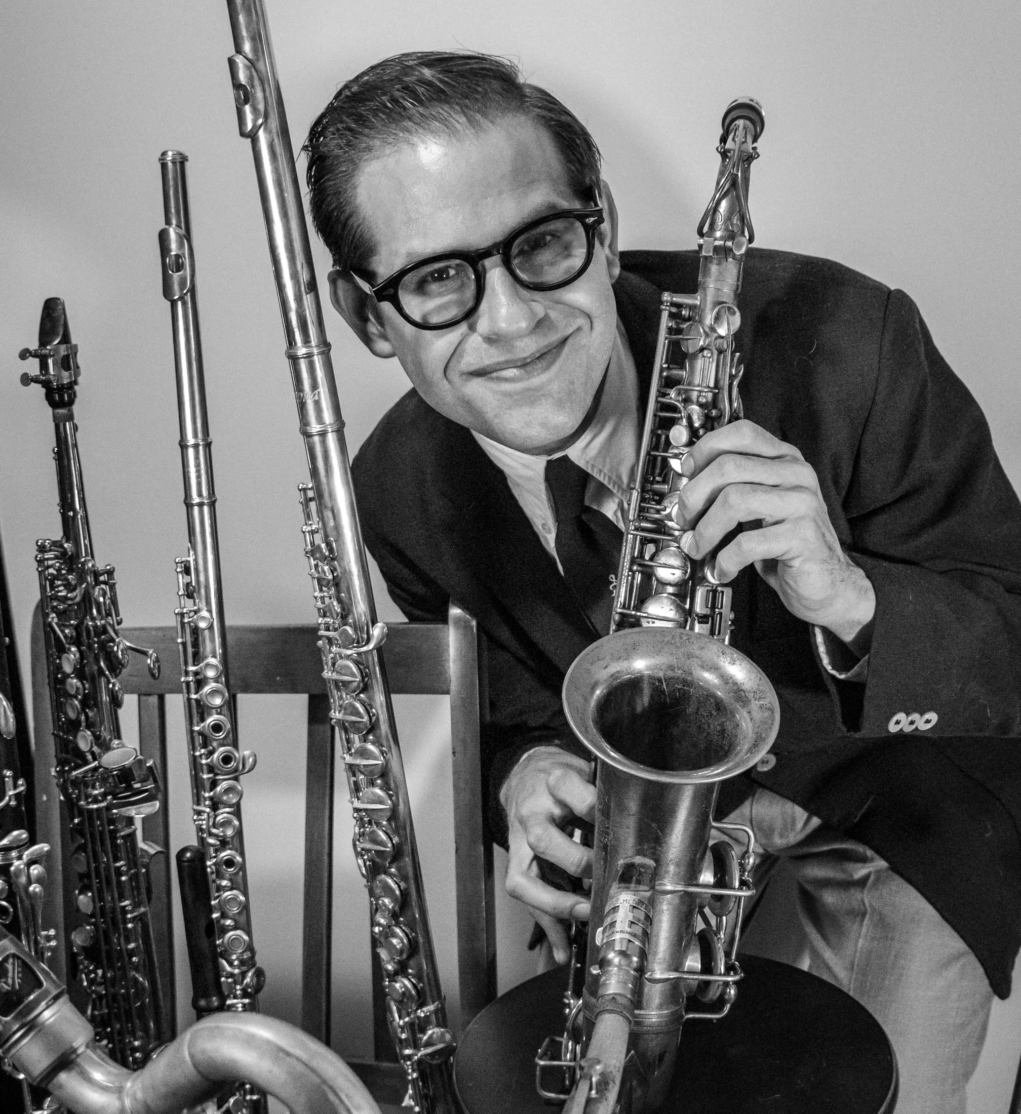 Close black and white portrait of Aaron Johnson leaning on a saxophone and smiling.