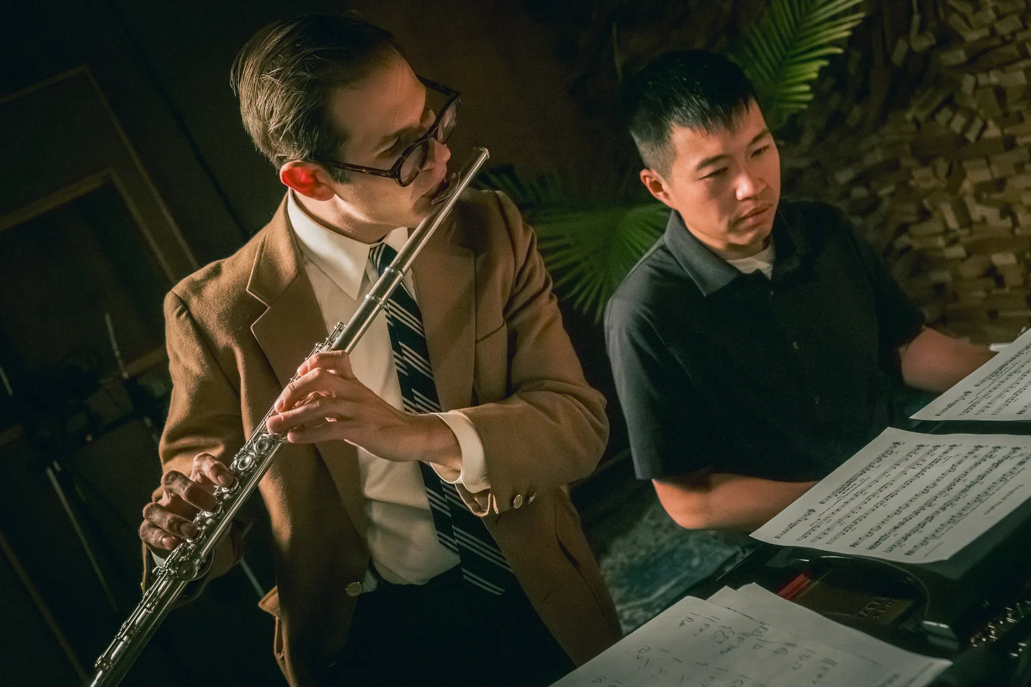 Aaron Johnson holding a flute and reading a score over the shoulder of a pianist during a recording session.