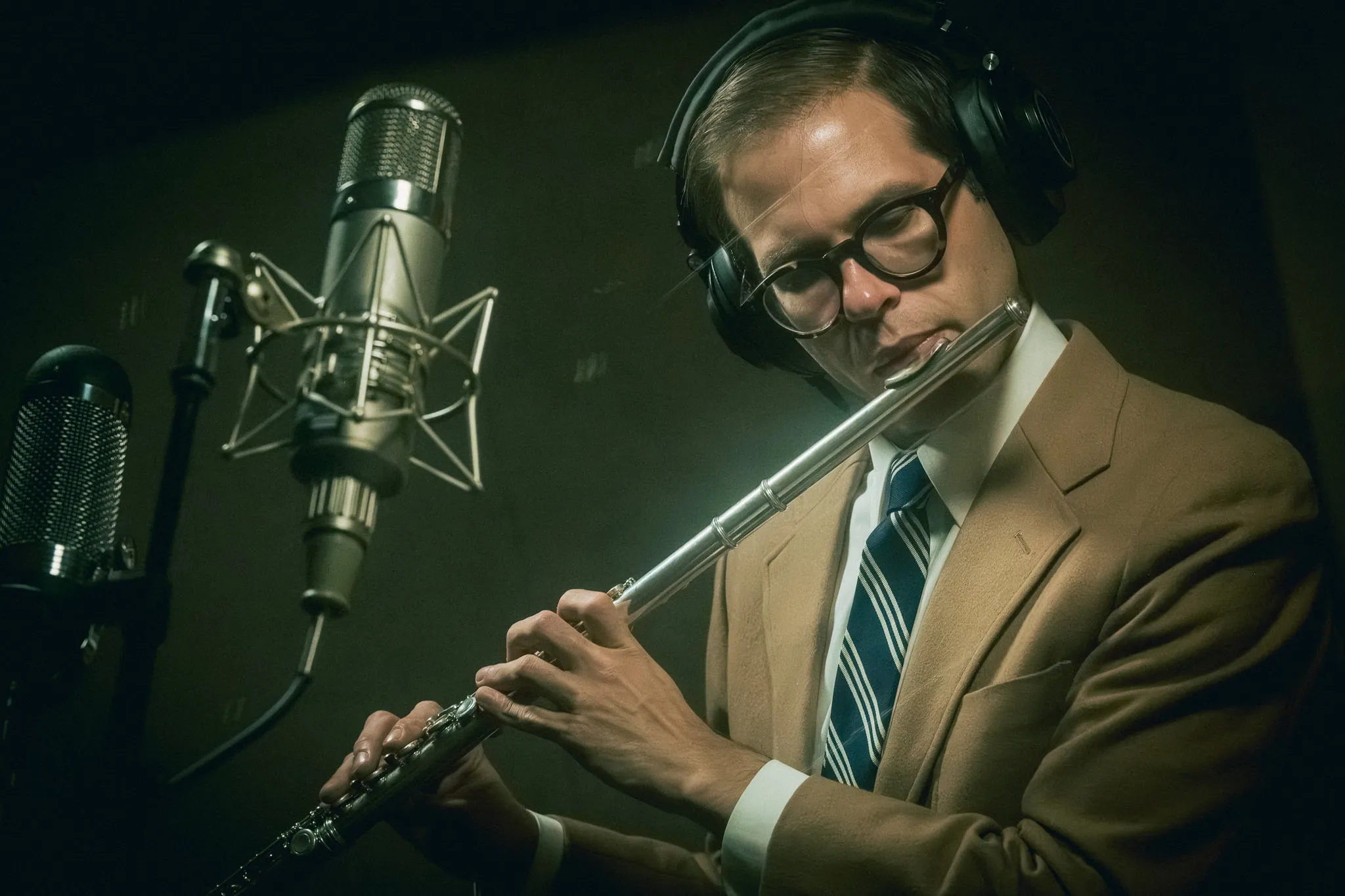 Aaron Johnson playing flute into a vintage ribbon microphone, lit against a dark studio.