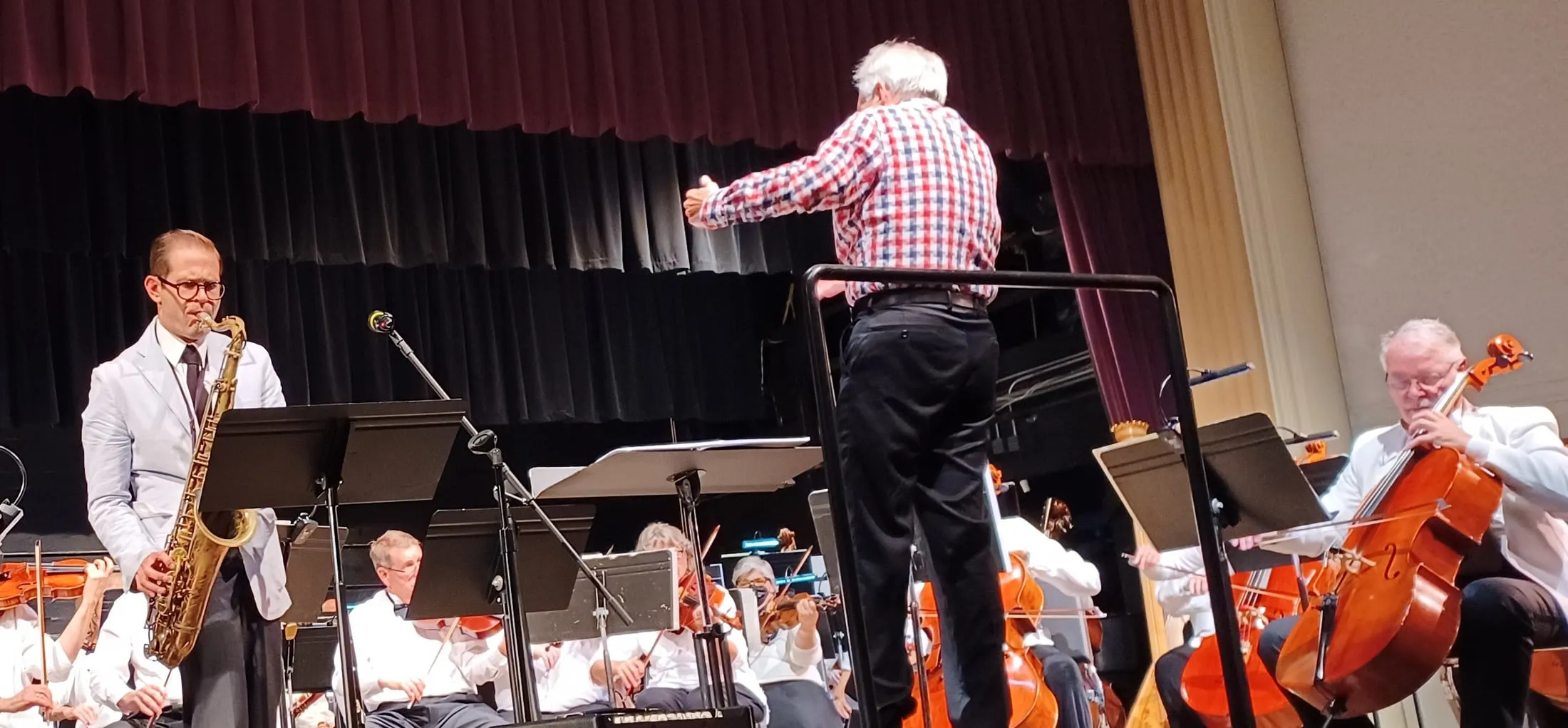 Aaron Johnson in the woodwind section of an orchestra, the conductor mid-downbeat.