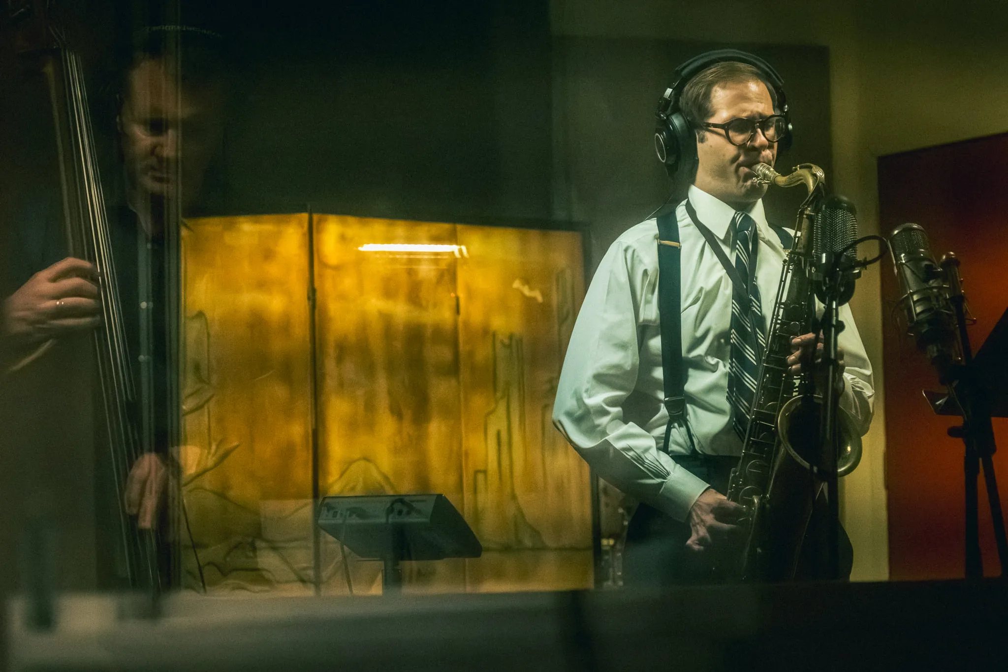 Aaron Johnson on tenor saxophone seen through studio glass at Samurai Hotel, a bassist reflected alongside him.