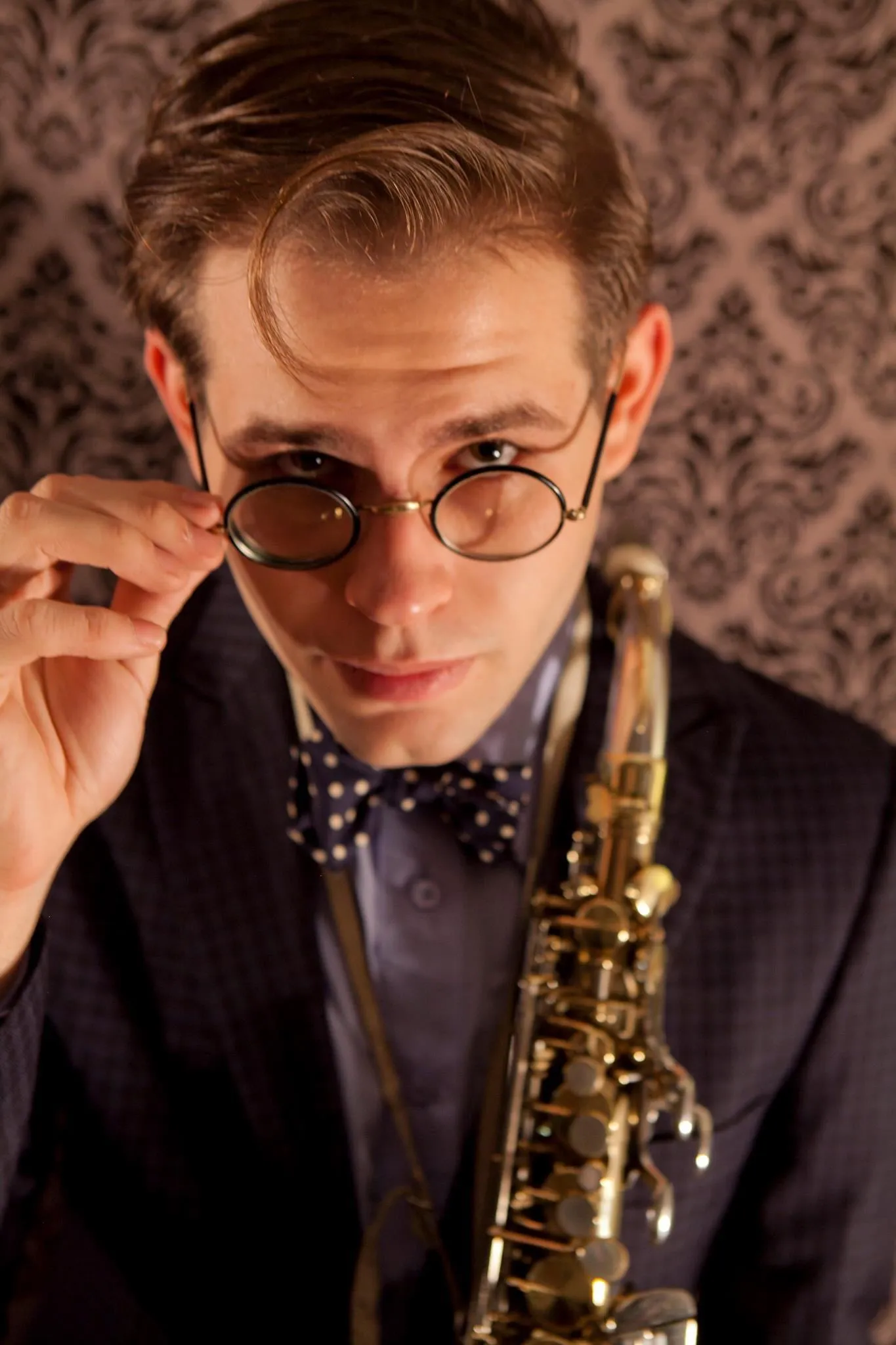 Aaron Johnson tilting a pair of round glasses, a soprano saxophone across his chest.
