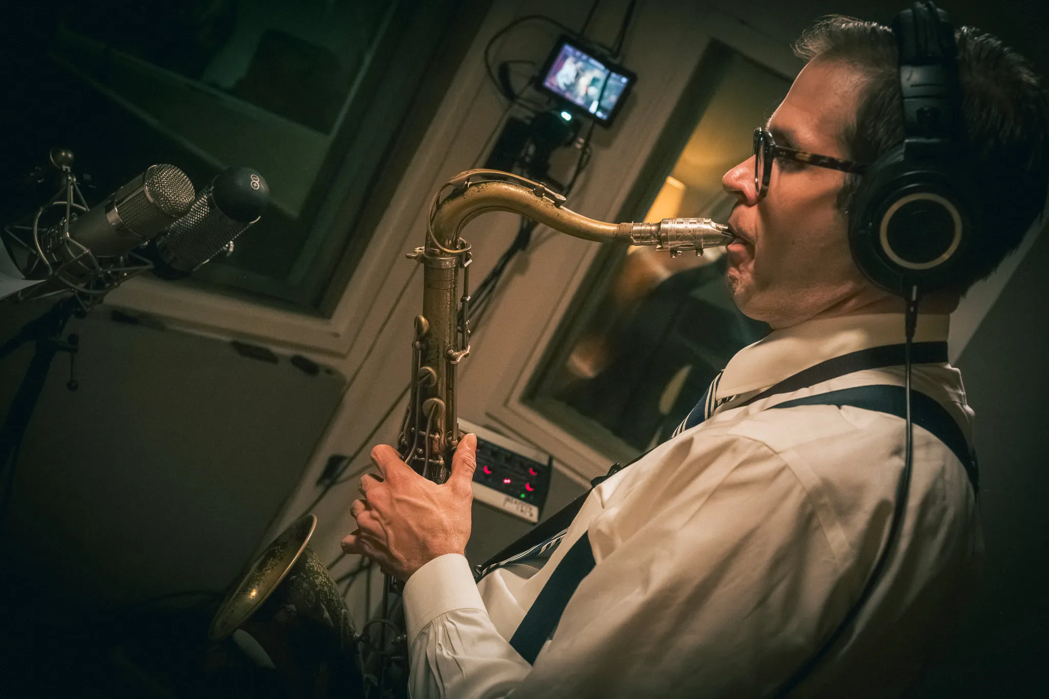 Aaron Johnson in headphones playing tenor saxophone into a studio microphone.
