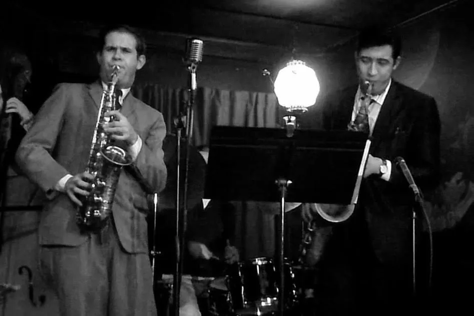 Black and white photograph of Aaron Johnson and another horn player at vintage stage microphones.